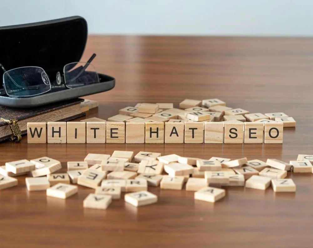 White Hat SEO concept shown with wooden letter blocks on a table with glasses and notebook