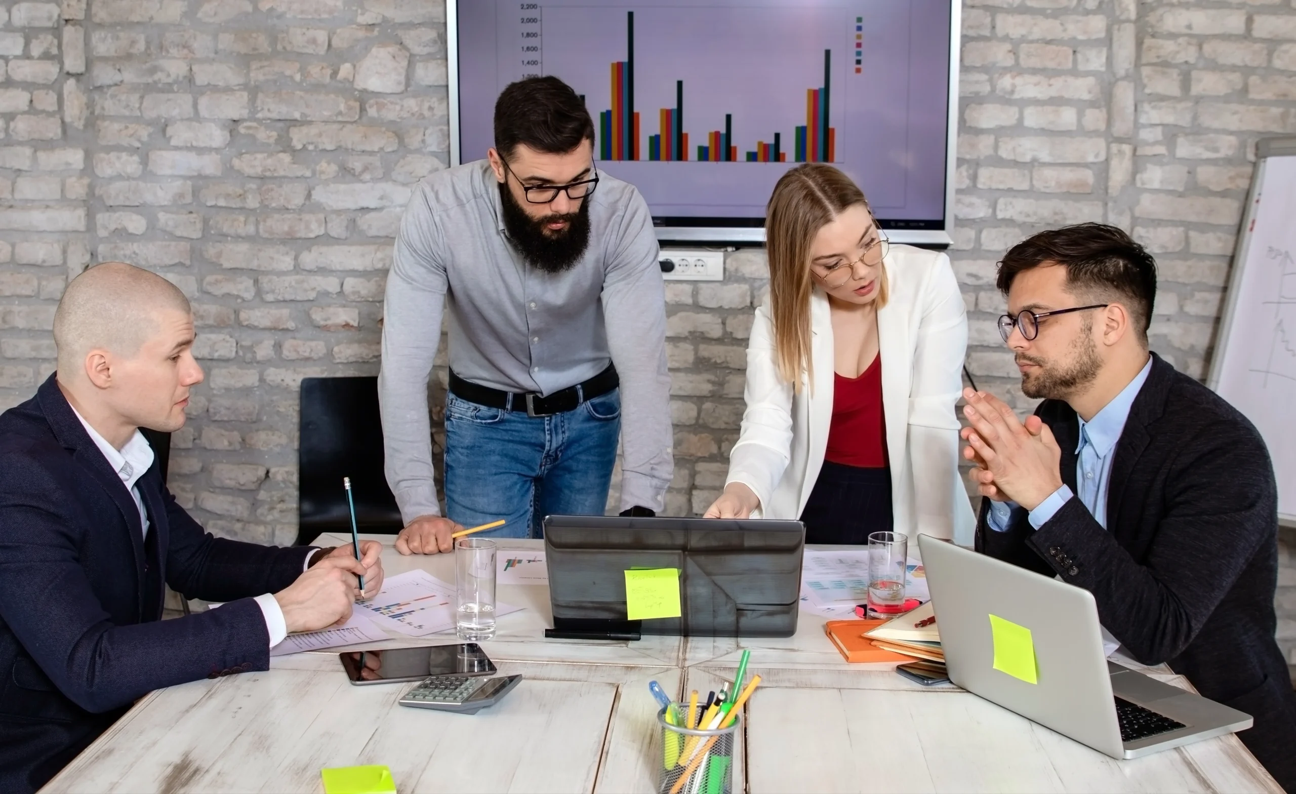 Team of four professionals discussing business strategies around a table with laptops, documents, and charts in the background