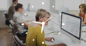 Business professionals working in an office with computers, a smiling woman in the foreground analyzing financial data on a monitor with a clock overlay.